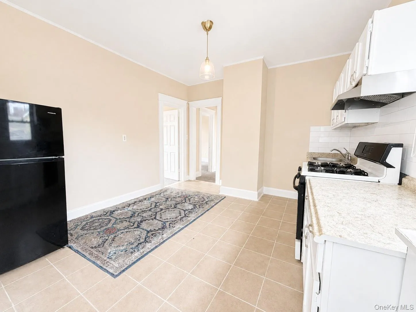Tan tiled flooring, white cabinetry, light-toned countertops, subway tile backsplash, and a modern pendant light fixture Tan tiled flooring, white cabinetry, light-toned countertops, subway tile backsplash, and a modern pendant light fixture