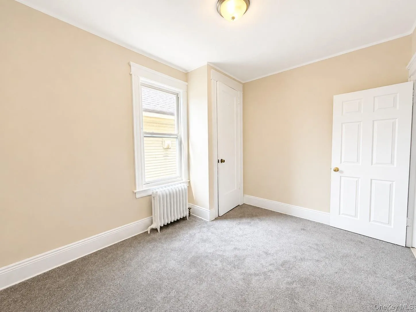 Neutral-toned carpeting, window with trim, white interior doors, and a ceiling-mounted light fixture Neutral-toned carpeting, window with trim, white interior doors, and a ceiling-mounted light fixture