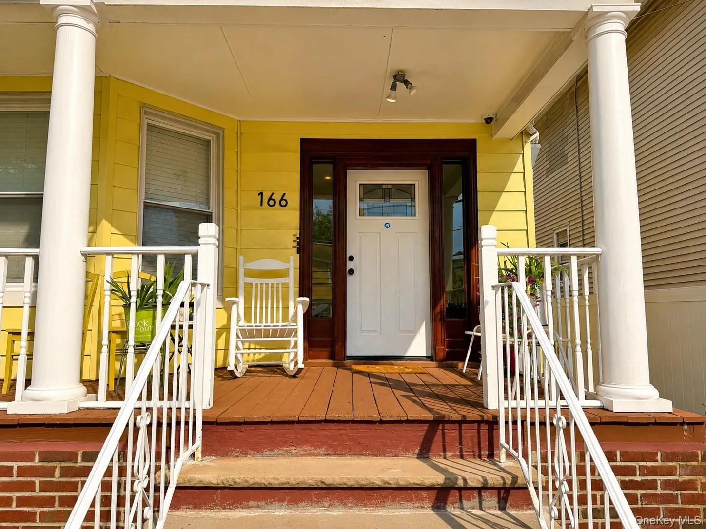 Inviting front porch featuring a white entry door with a sidelight, rich wood-tone trim, and decorative white railings Inviting front porch featuring a white entry door with a sidelight, rich wood-tone trim, and decorative white railings