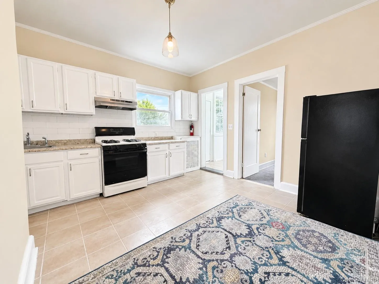 Kitchen featuring white cabinetry, subway tile backsplash, light-colored tile flooring, and a window Kitchen featuring white cabinetry, subway tile backsplash, light-colored tile flooring, and a window