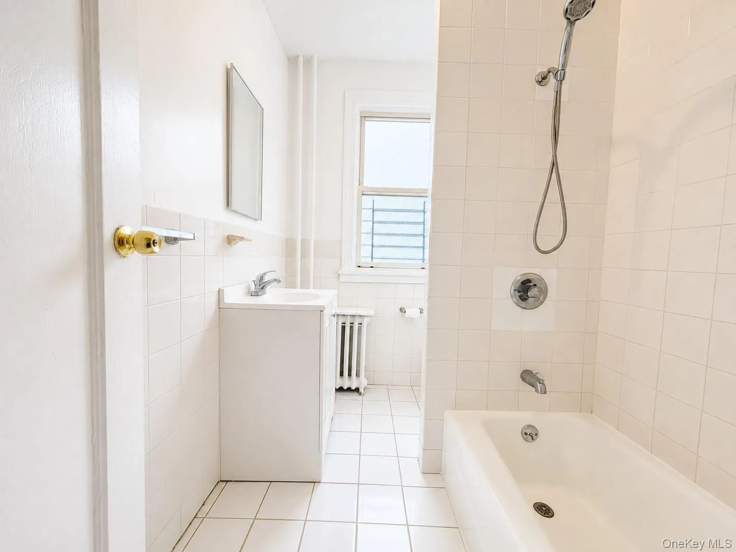 White tiled bathroom featuring a built-in bathtub with shower, vanity with sink, and a window White tiled bathroom featuring a built-in bathtub with shower, vanity with sink, and a window