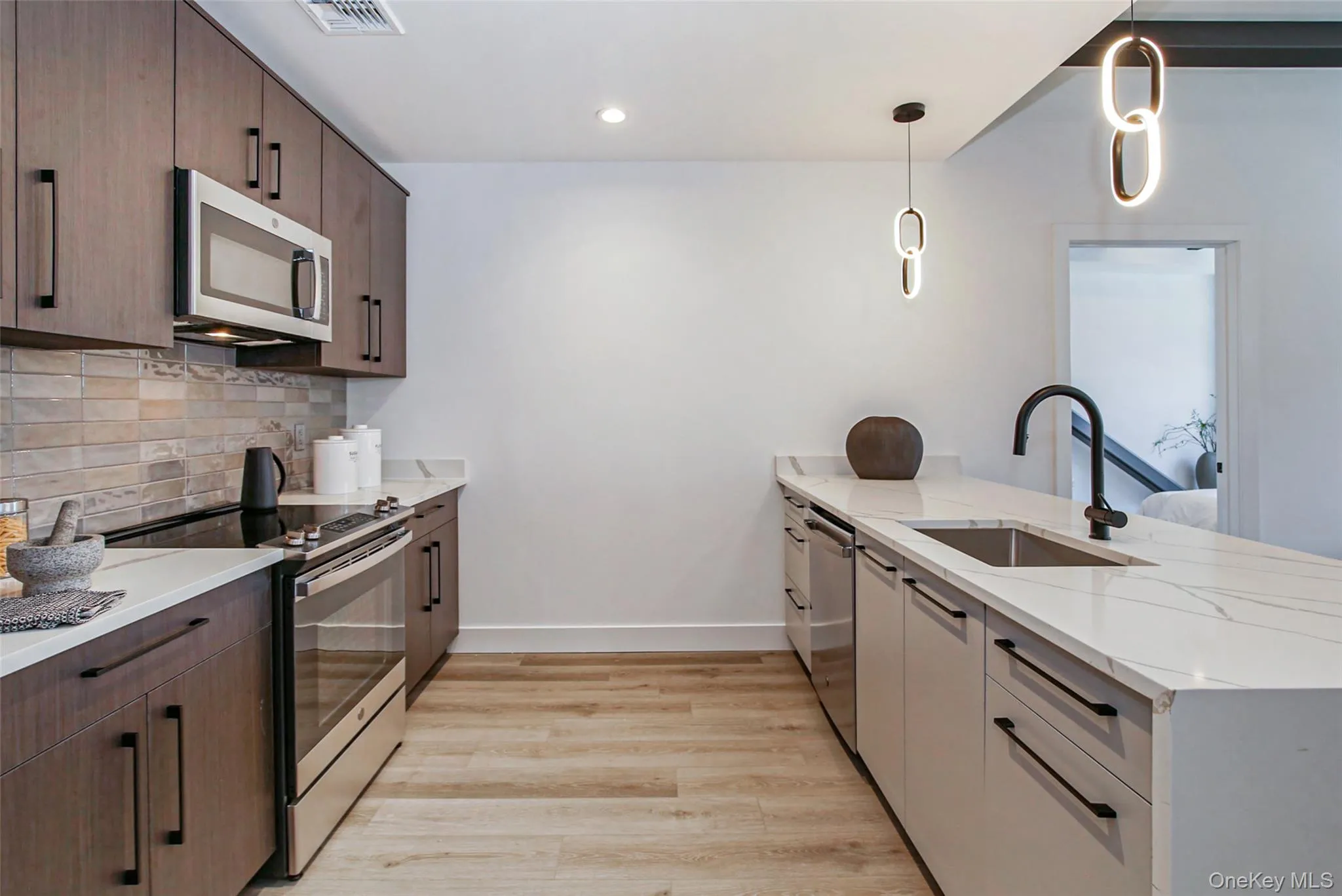 Kitchen featuring appliances with stainless steel finishes, a peninsula, tasteful backsplash, light wood finished floors, and light stone countertops Kitchen featuring appliances with stainless steel finishes, a peninsula, tasteful backsplash, light wood finished floors, and light stone countertops