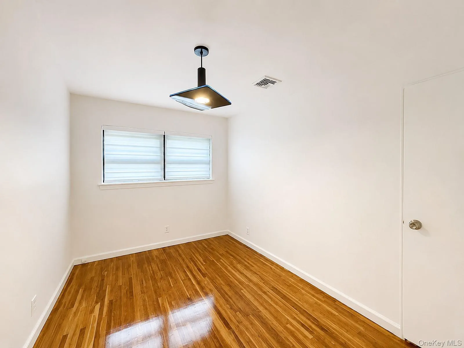 Polished wood flooring, modern pendant light fixture, window with privacy blinds, white door with brushed nickel hardware, and a ceiling-mounted register Polished wood flooring, modern pendant light fixture, window with privacy blinds, white door with brushed nickel hardware, and a ceiling-mounted register