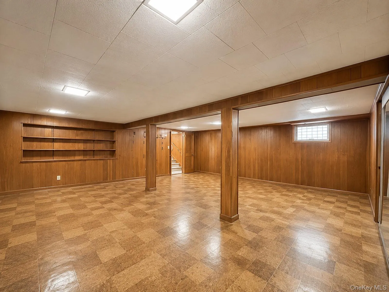 Expansive room featuring wood-paneled walls, built-in shelving, tiled flooring, and multiple ceiling-mounted light fixtures Expansive room featuring wood-paneled walls, built-in shelving, tiled flooring, and multiple ceiling-mounted light fixtures
