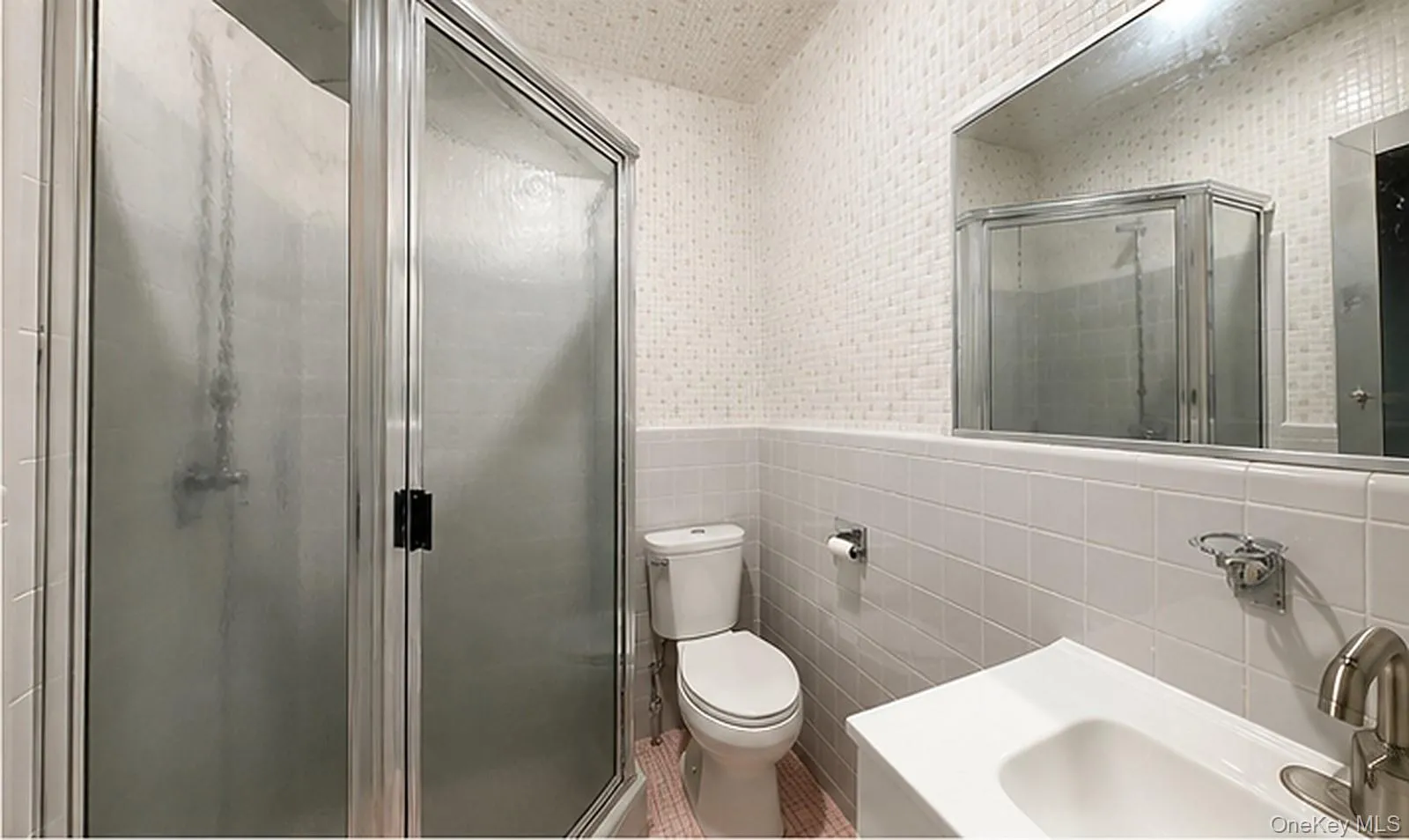 Chrome-framed glass shower enclosure, white ceramic tile walls, integrated vanity sink, and a wall-mounted mirror Chrome-framed glass shower enclosure, white ceramic tile walls, integrated vanity sink, and a wall-mounted mirror