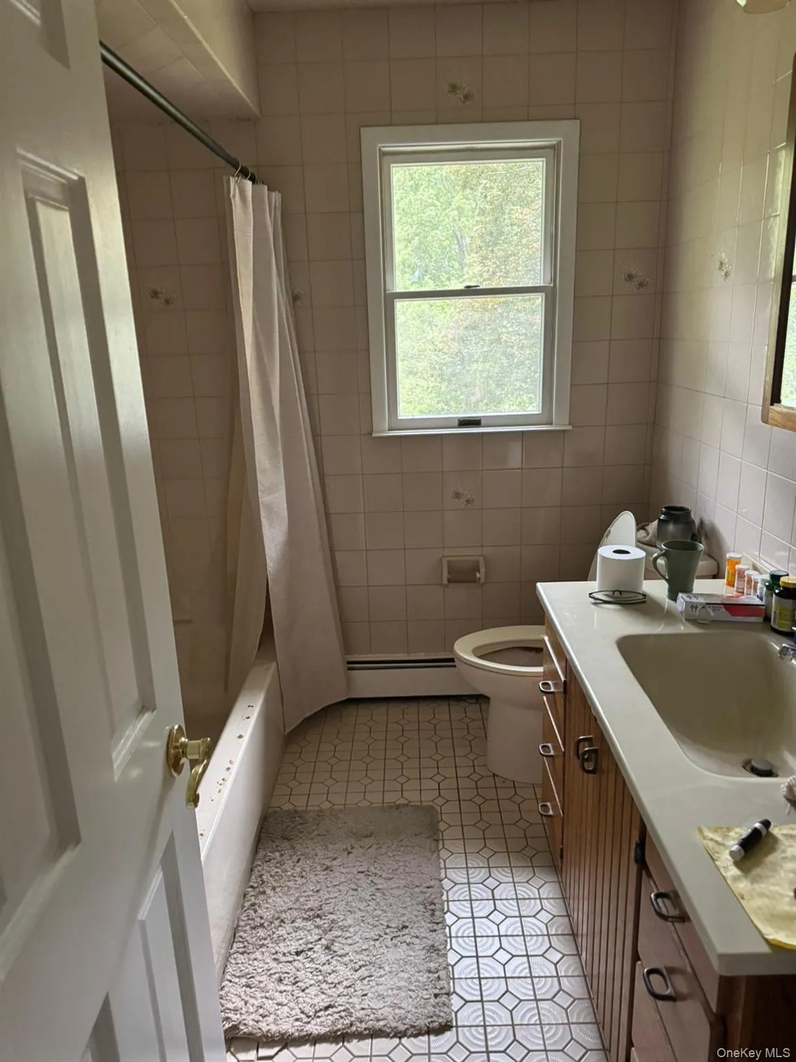 Full bath with vanity, shower / tub combo with curtain, a baseboard heating unit, tile walls, and light tile patterned floors Full bath with vanity, shower / tub combo with curtain, a baseboard heating unit, tile walls, and light tile patterned floors