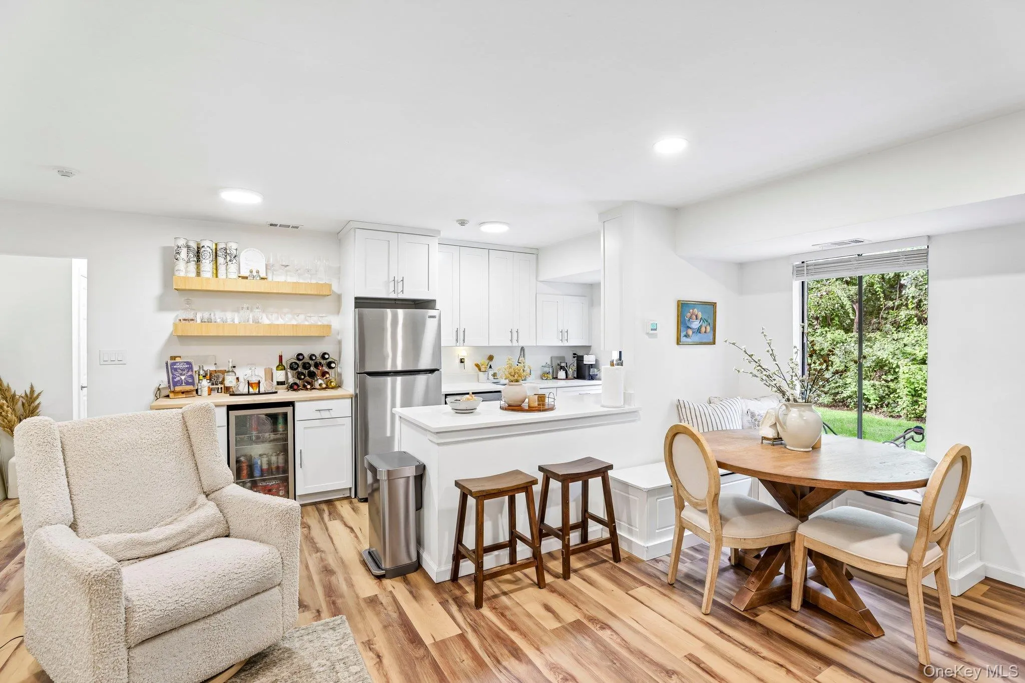 The space flows naturally into the classic kitchen, featuring white Shaker cabinetry, stainless steel appliances, quartz countertops, and a custom cafe center with a built-mini fridge The space flows naturally into the classic kitchen, featuring white Shaker cabinetry, stainless steel appliances, quartz countertops, and a custom cafe center with a built-mini fridge