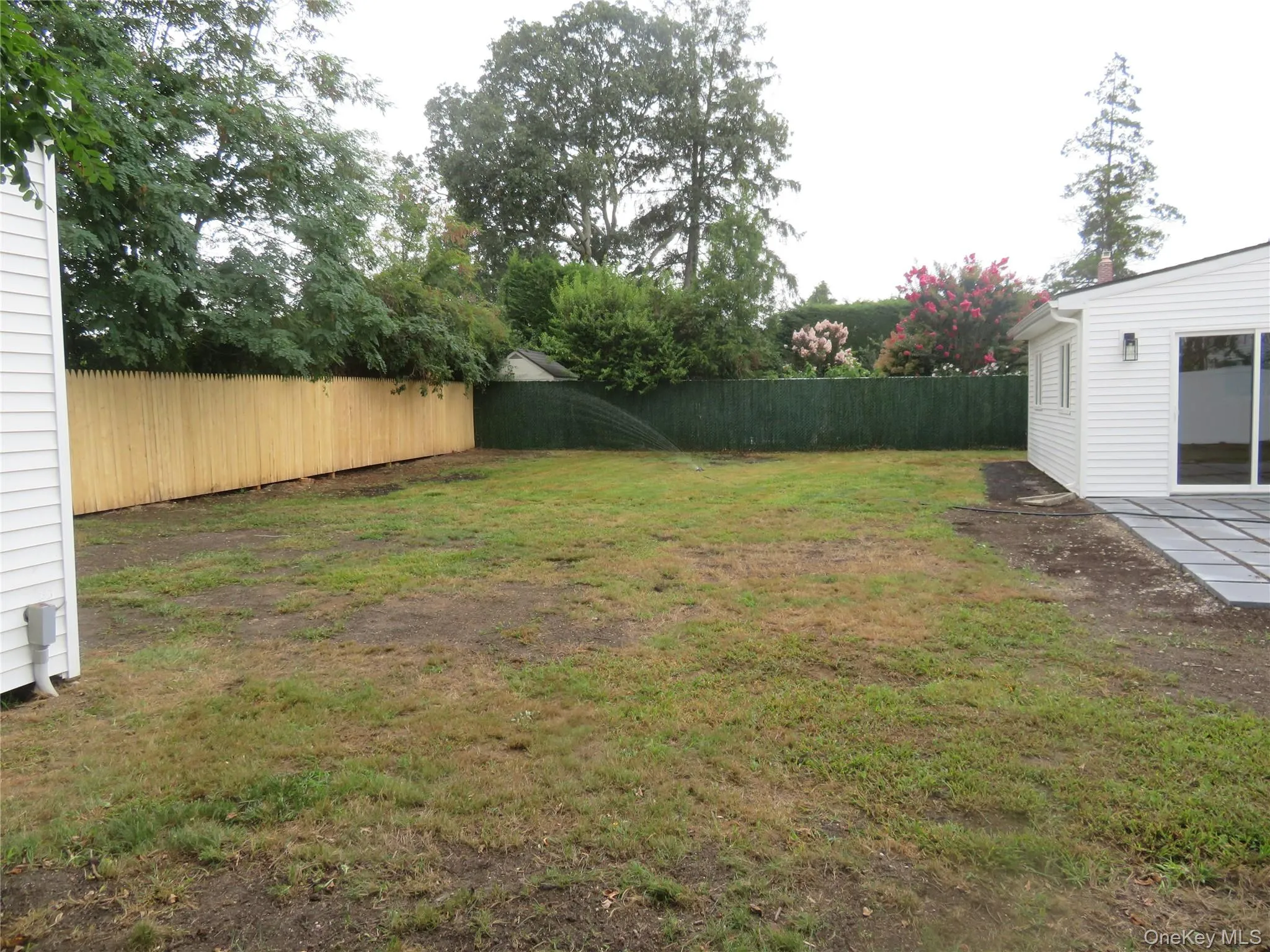 Expansive backyard with a new wood picket fence, a privacy screen, and a newly installed paver patio Expansive backyard with a new wood picket fence, a privacy screen, and a newly installed paver patio