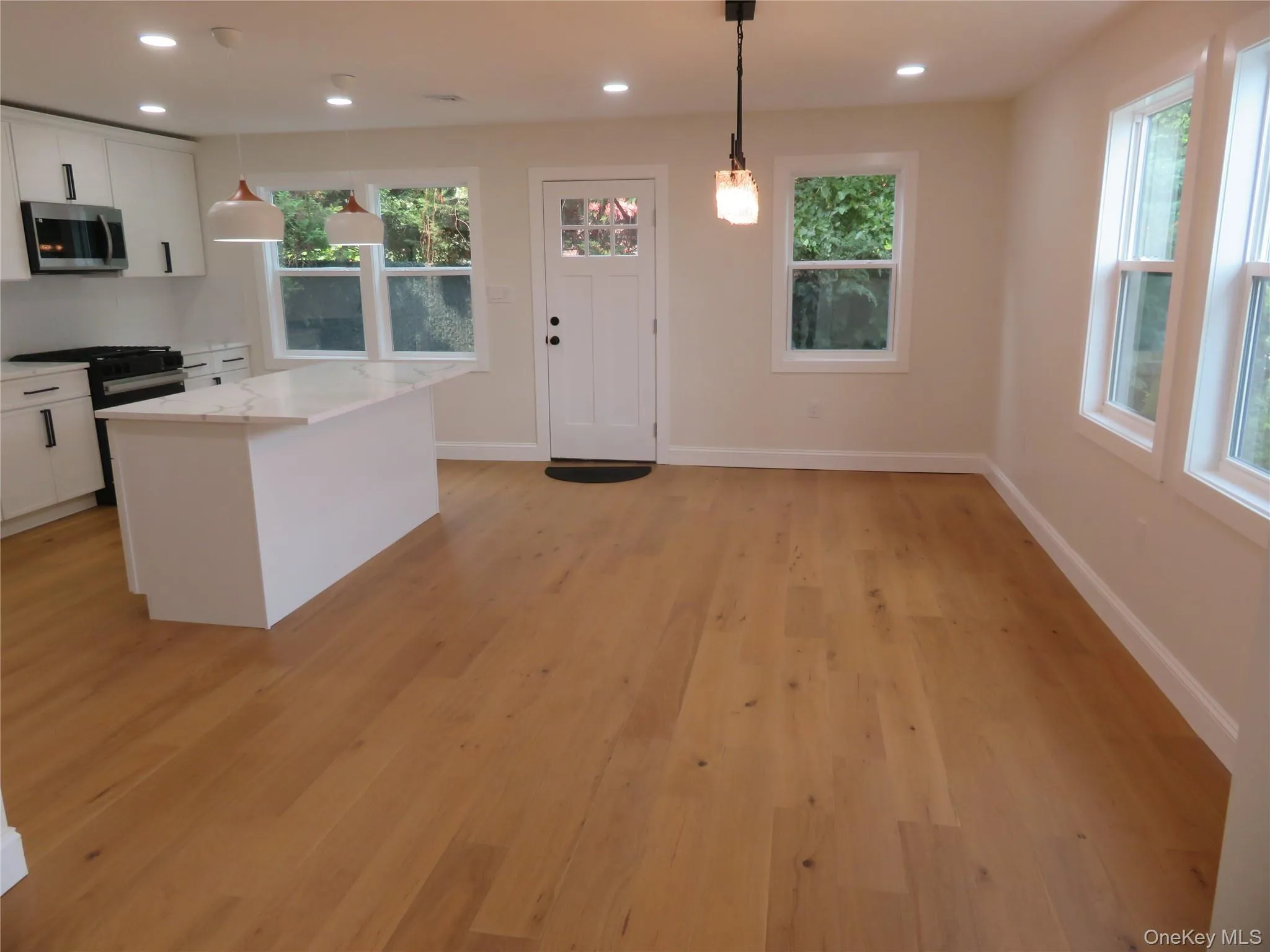 Hardwood-style flooring, white shaker cabinets, stainless steel appliances, kitchen island with stone-finish countertop, and recessed lighting Hardwood-style flooring, white shaker cabinets, stainless steel appliances, kitchen island with stone-finish countertop, and recessed lighting