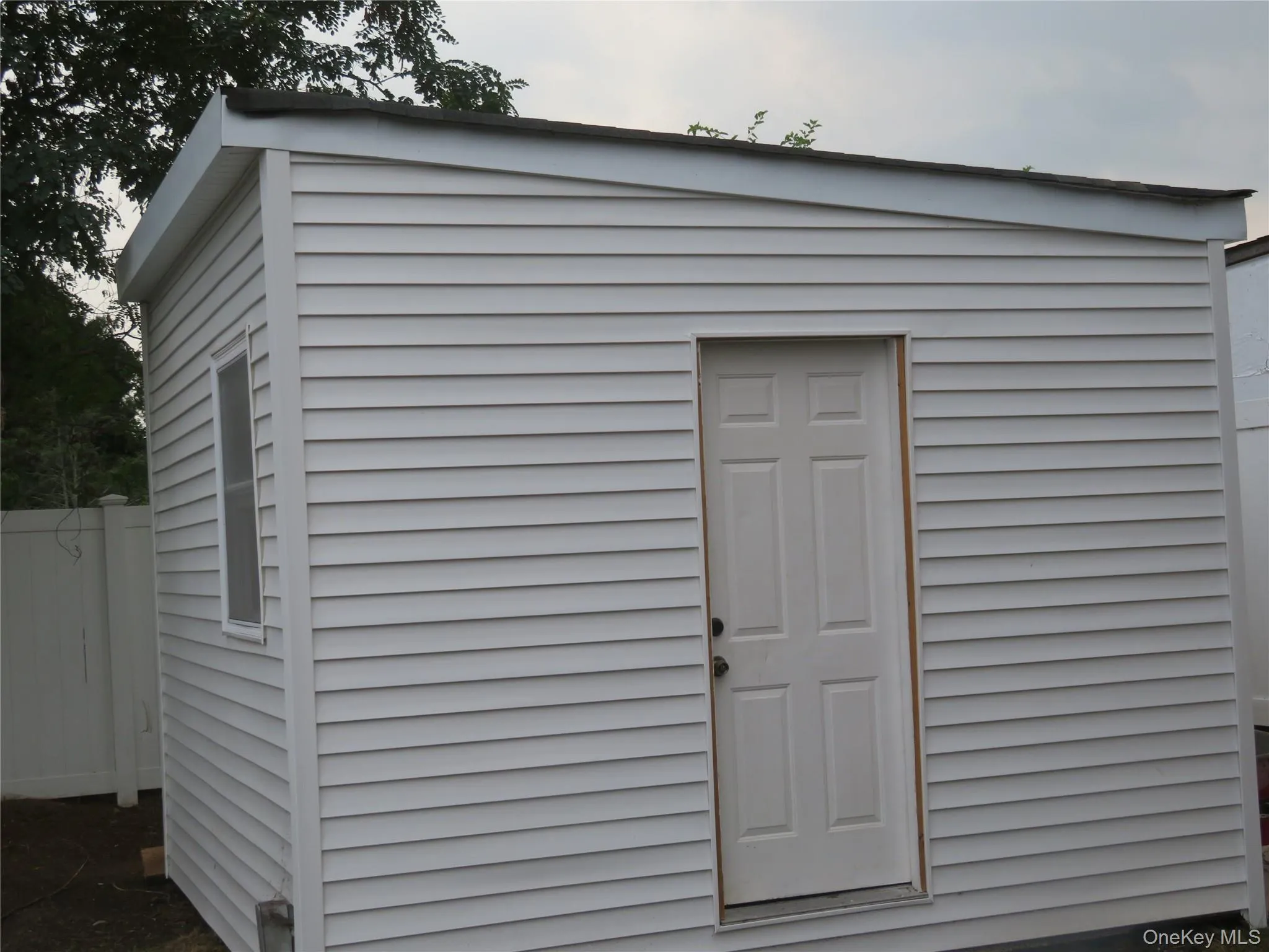 White horizontal siding structure with a single window and a paneled door White horizontal siding structure with a single window and a paneled door