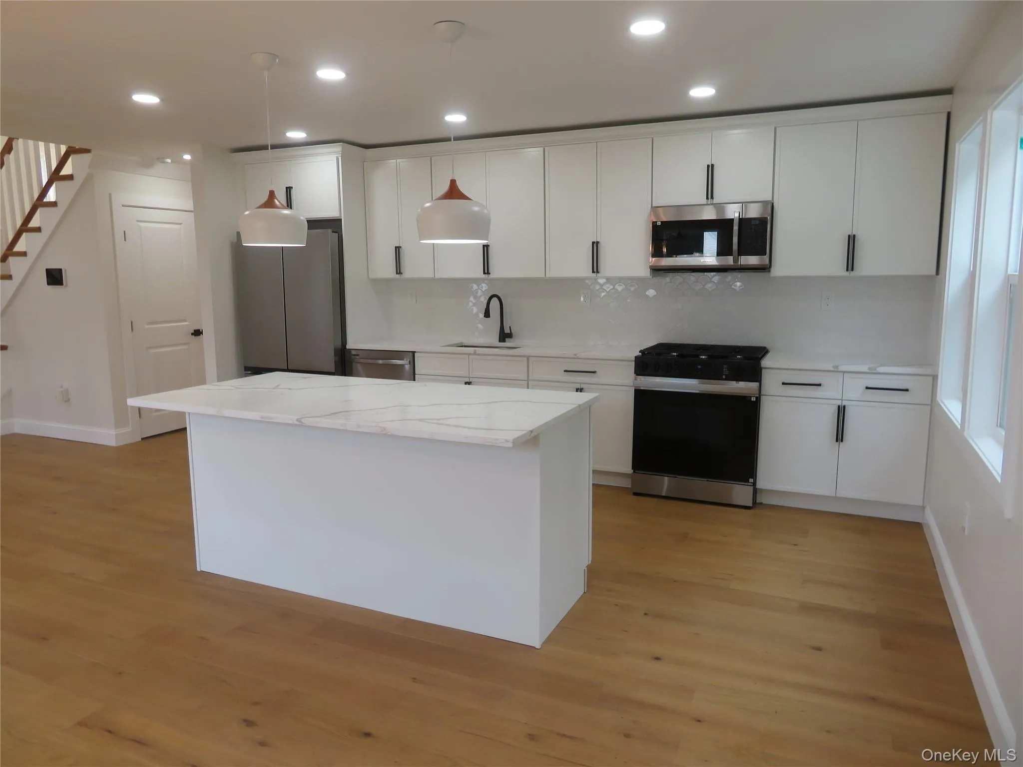 Kitchen featuring wood-finish flooring, a central island with a stone countertop, white cabinetry with black hardware, stainless steel appliances, and recessed lighting Kitchen featuring wood-finish flooring, a central island with a stone countertop, white cabinetry with black hardware, stainless steel appliances, and recessed lighting