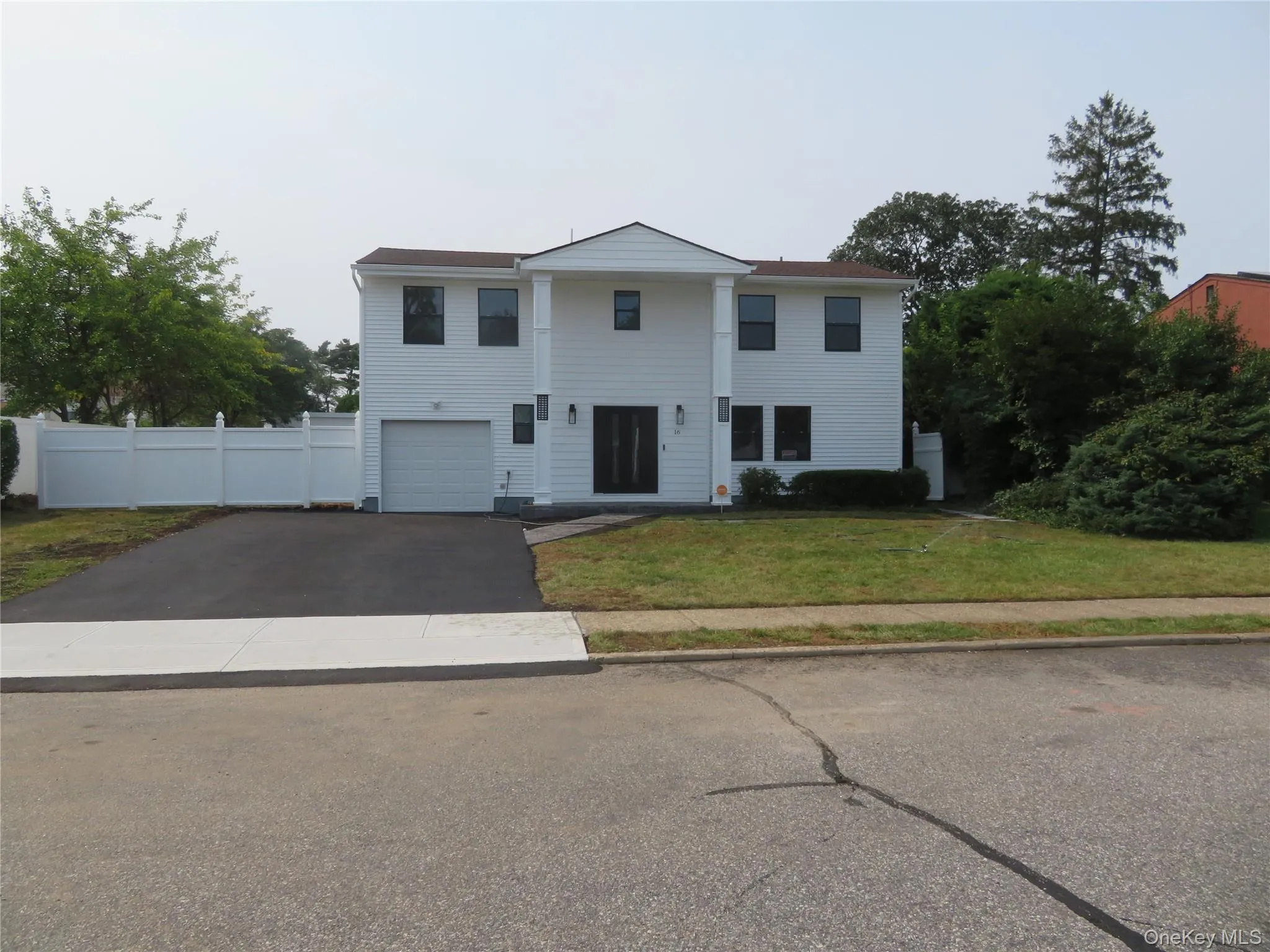 Two-story residence featuring white siding, a paved driveway, an attached garage, a white privacy fence, and a front lawn Two-story residence featuring white siding, a paved driveway, an attached garage, a white privacy fence, and a front lawn