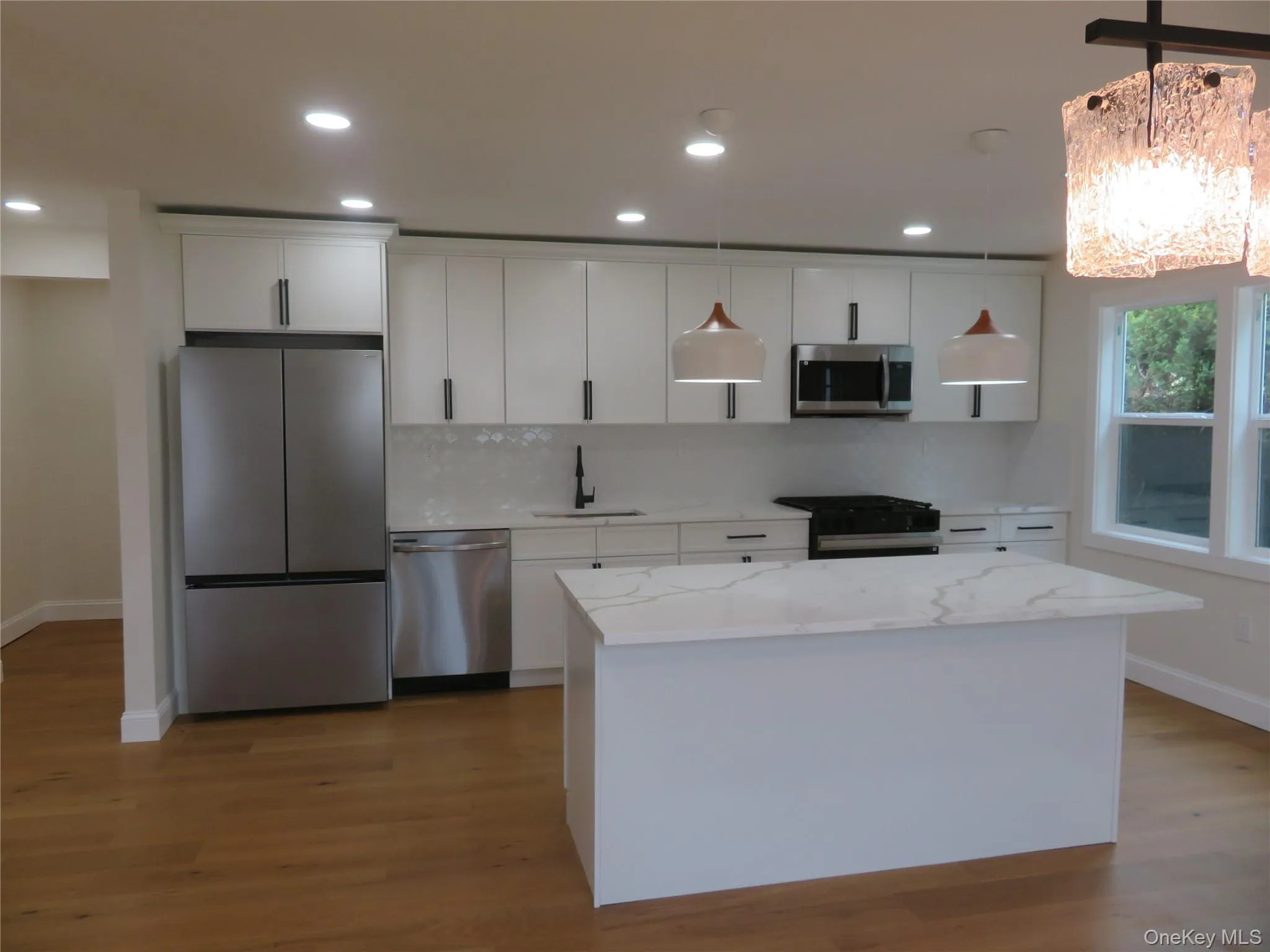 Contemporary kitchen featuring white cabinetry, stainless steel appliances, a center island with a light-toned countertop, and recessed lighting Contemporary kitchen featuring white cabinetry, stainless steel appliances, a center island with a light-toned countertop, and recessed lighting