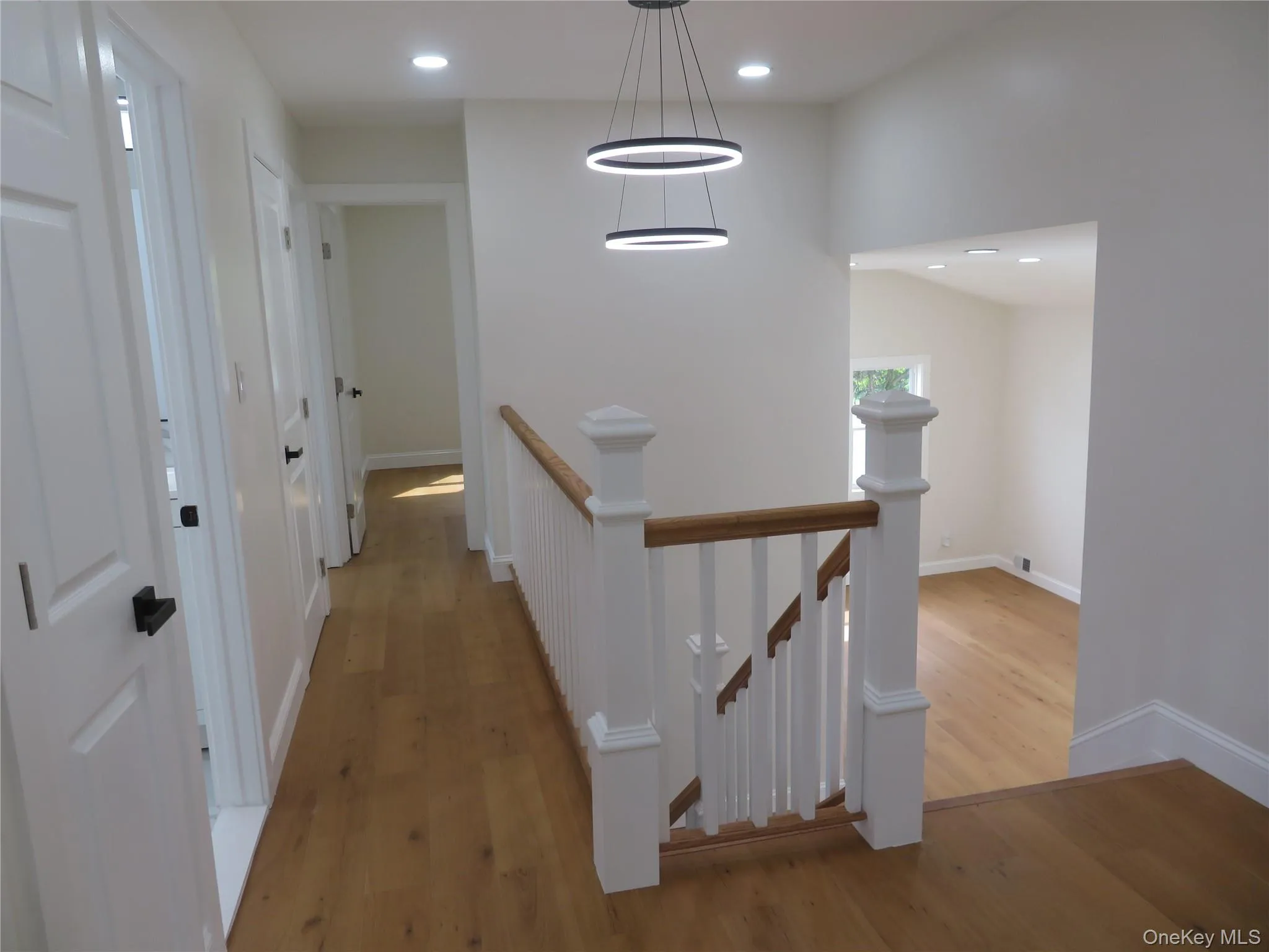 Wood-finish flooring, white paneled doors with matte black hardware, recessed lighting, and a contemporary multi-ring chandelier Wood-finish flooring, white paneled doors with matte black hardware, recessed lighting, and a contemporary multi-ring chandelier