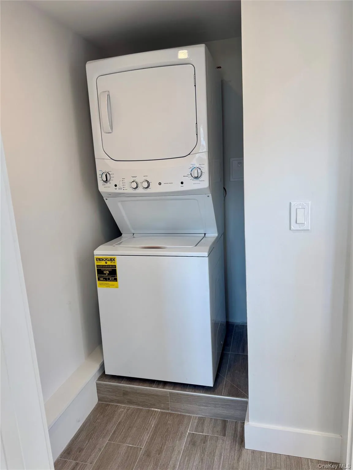Stackable washer and dryer unit, integrated within a tiled alcove featuring wood-styled flooring Stackable washer and dryer unit, integrated within a tiled alcove featuring wood-styled flooring