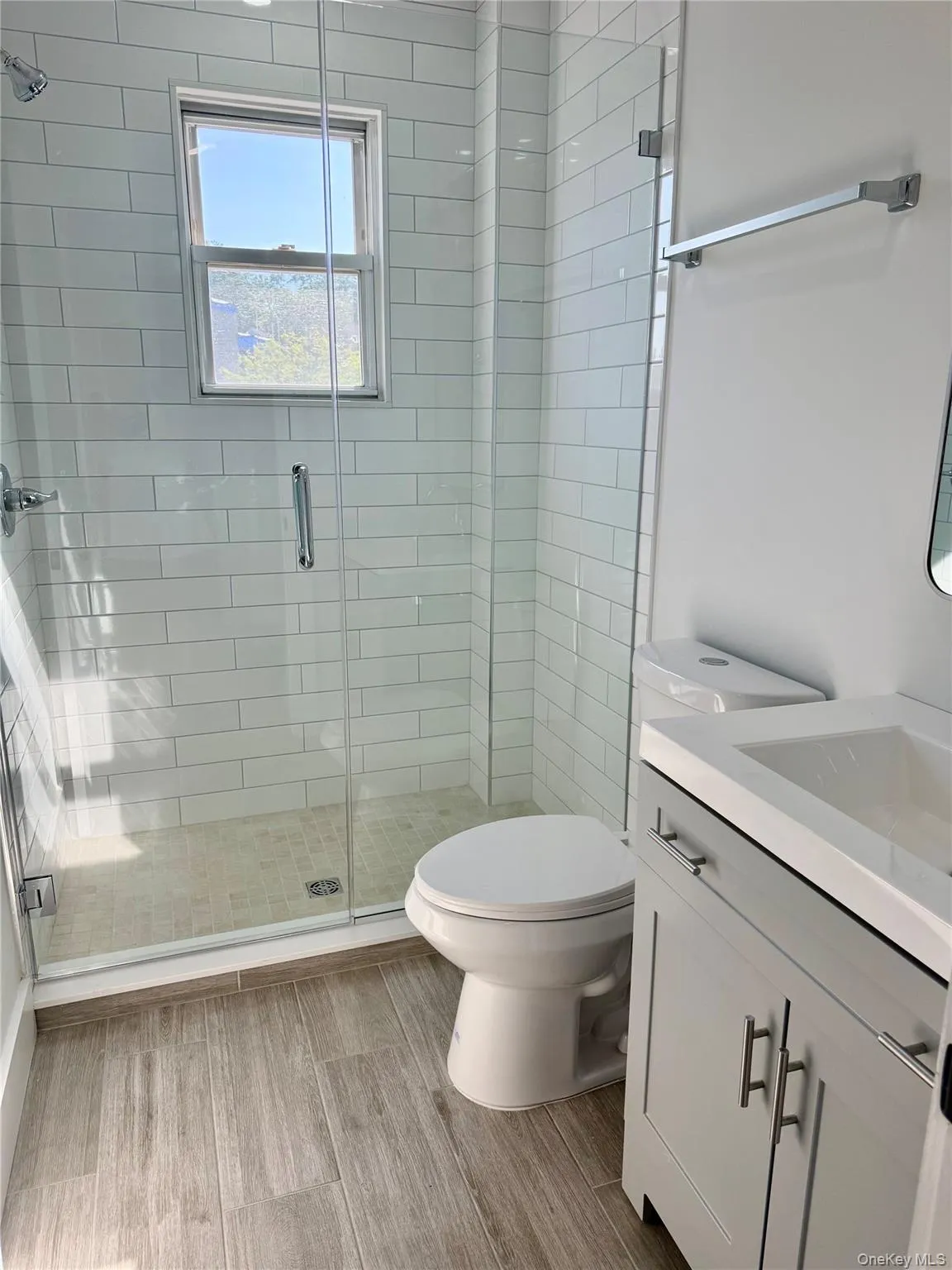 Glass-enclosed shower with white subway tile, wood-styled flooring, and a vanity with storage Glass-enclosed shower with white subway tile, wood-styled flooring, and a vanity with storage