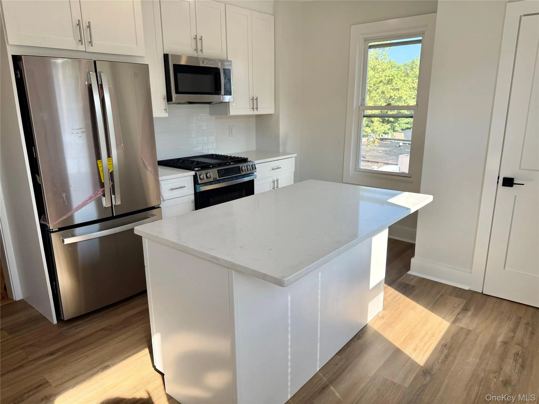 White shaker cabinetry, stainless steel appliances, white subway tile backsplash, white center island, and wood-finish flooring White shaker cabinetry, stainless steel appliances, white subway tile backsplash, white center island, and wood-finish flooring