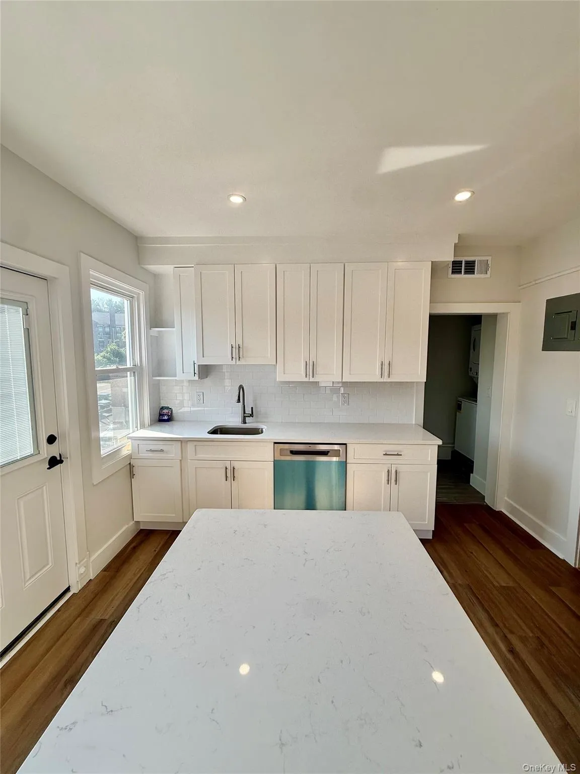 Kitchen featuring white shaker cabinetry, white countertops, wood-finish flooring, a stainless steel dishwasher, and recessed lighting Kitchen featuring white shaker cabinetry, white countertops, wood-finish flooring, a stainless steel dishwasher, and recessed lighting