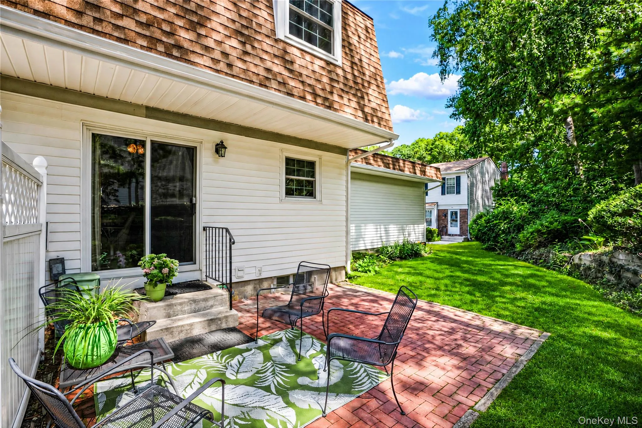 Backyard patio with brick hardscaping, leading to a manicured lawn and mature trees Backyard patio with brick hardscaping, leading to a manicured lawn and mature trees