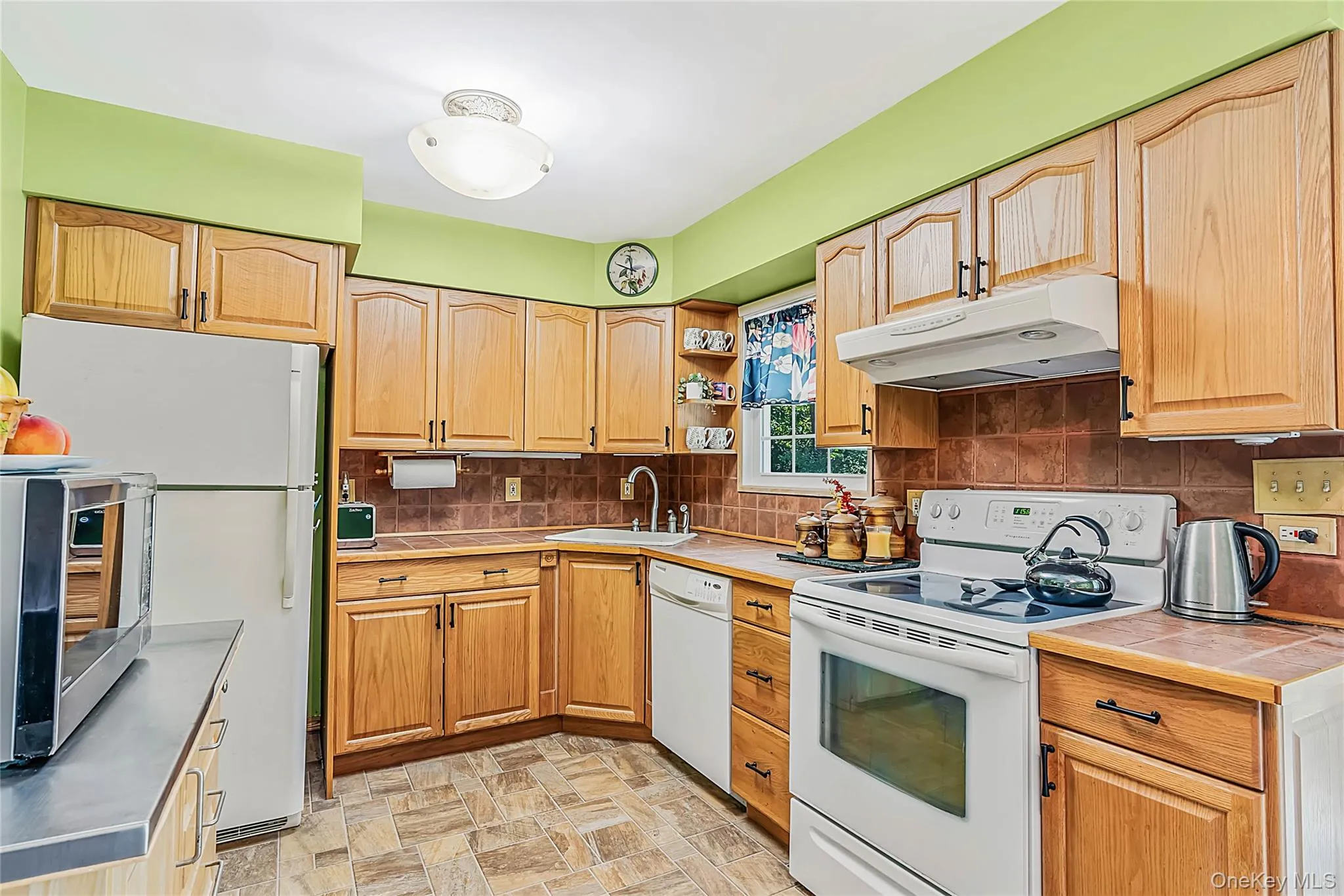 Wood-finish cabinetry, tile flooring, ceramic tile backsplash, white range, and recessed sink Wood-finish cabinetry, tile flooring, ceramic tile backsplash, white range, and recessed sink