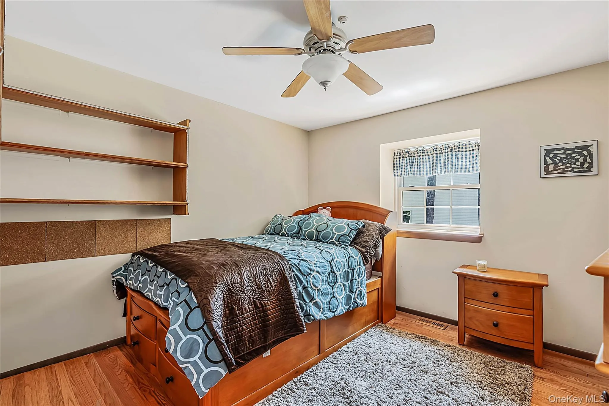 Wood-finish flooring, built-in shelving, ceiling fan, and a window with trim Wood-finish flooring, built-in shelving, ceiling fan, and a window with trim