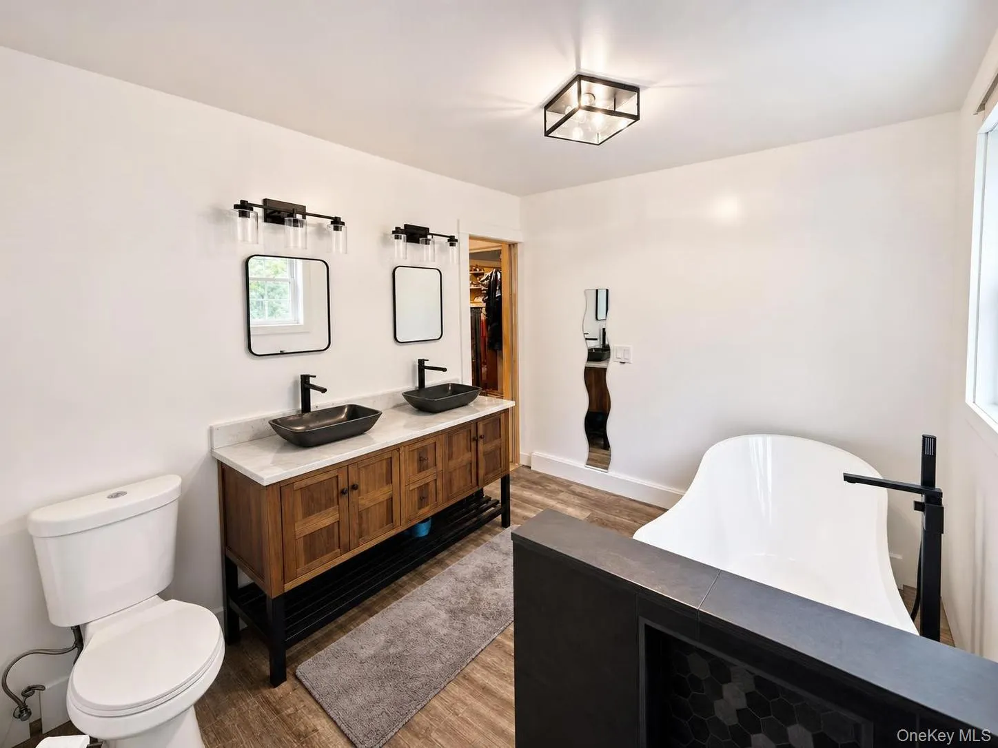 Dual vanity with vessel sinks and black fixtures, freestanding soaking tub, wood-finish flooring, and a tiled walk-in shower Dual vanity with vessel sinks and black fixtures, freestanding soaking tub, wood-finish flooring, and a tiled walk-in shower