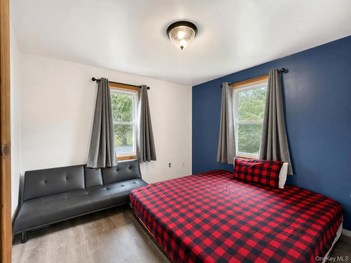 Room featuring two windows with wood trim, a ceiling-mounted light fixture, and wood-finish flooring Room featuring two windows with wood trim, a ceiling-mounted light fixture, and wood-finish flooring