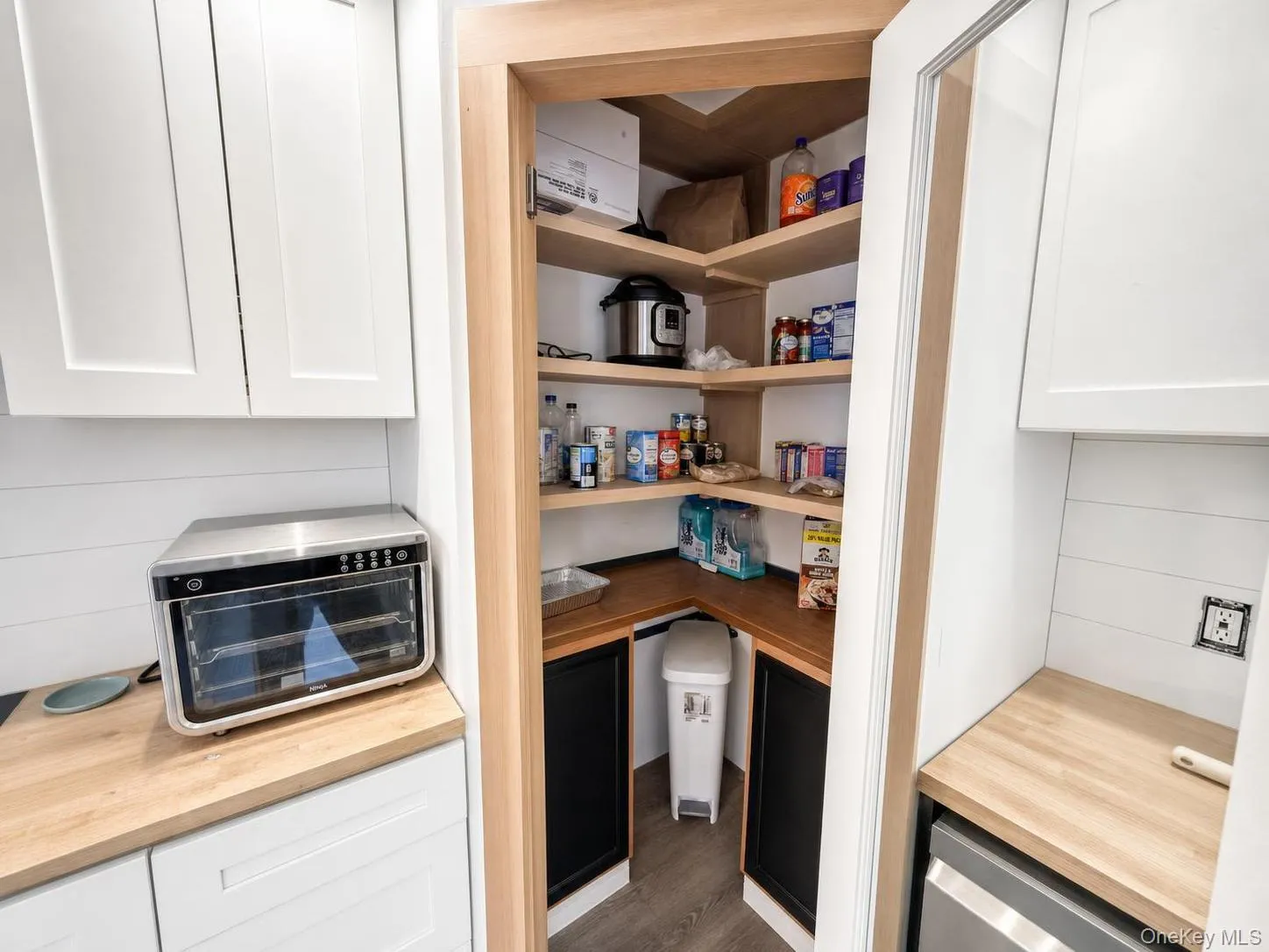 Corner pantry featuring wood-finish shelving and countertops, white cabinetry, and shiplap wall accents Corner pantry featuring wood-finish shelving and countertops, white cabinetry, and shiplap wall accents