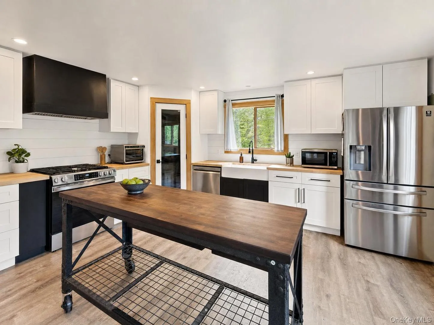 Contemporary kitchen featuring light wood-finish flooring, white cabinetry, wood countertops, a farmhouse sink, and stainless steel appliances Contemporary kitchen featuring light wood-finish flooring, white cabinetry, wood countertops, a farmhouse sink, and stainless steel appliances