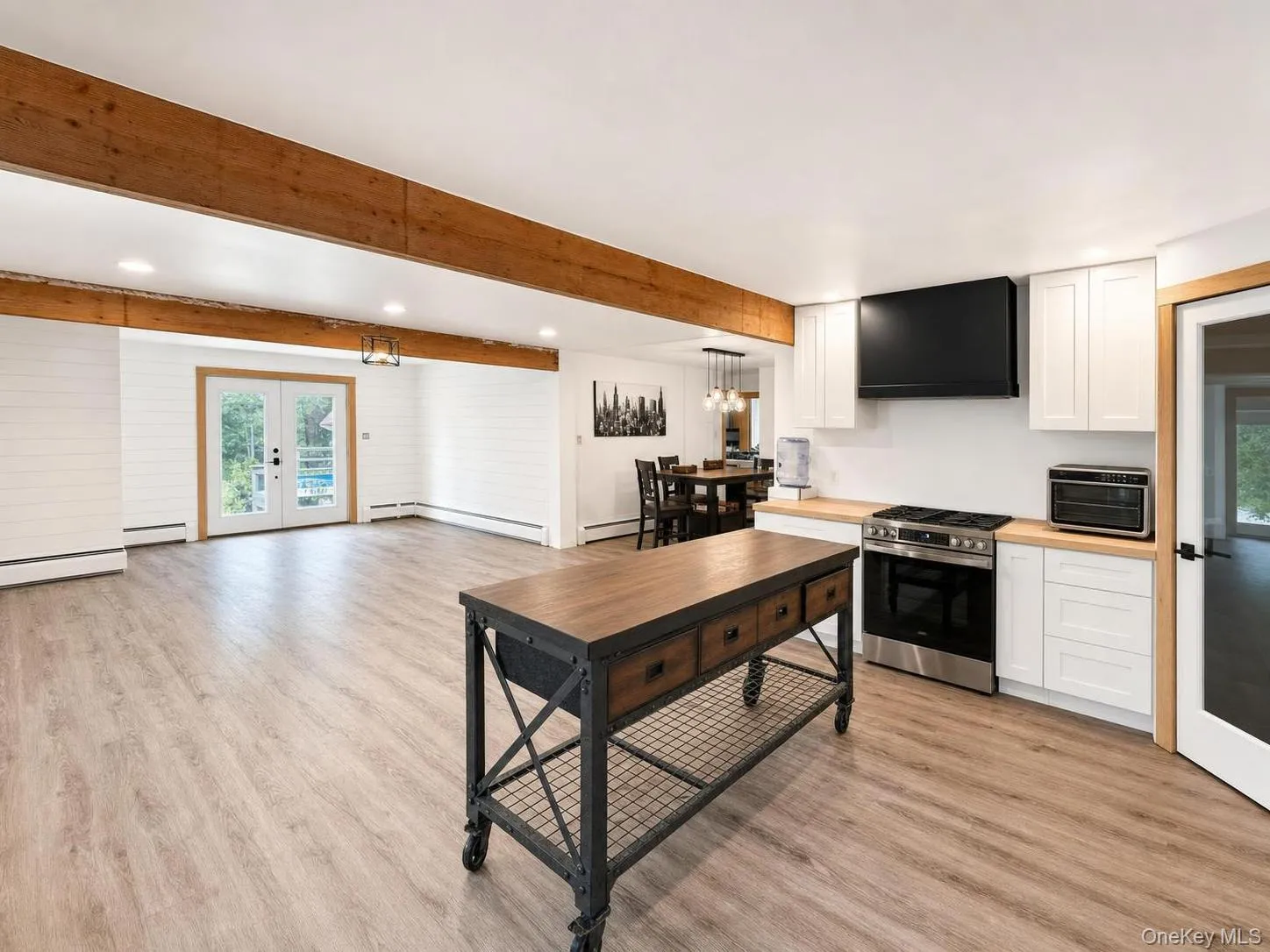 Wood-finish flooring throughout, white shiplap wall accents, exposed wood beams, and a kitchen island with storage Wood-finish flooring throughout, white shiplap wall accents, exposed wood beams, and a kitchen island with storage