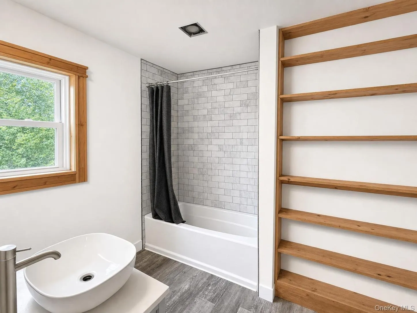 Bathroom featuring a white vessel sink, brushed nickel faucet, wood-finish flooring, built-in open shelving, and a tiled shower-tub combination Bathroom featuring a white vessel sink, brushed nickel faucet, wood-finish flooring, built-in open shelving, and a tiled shower-tub combination