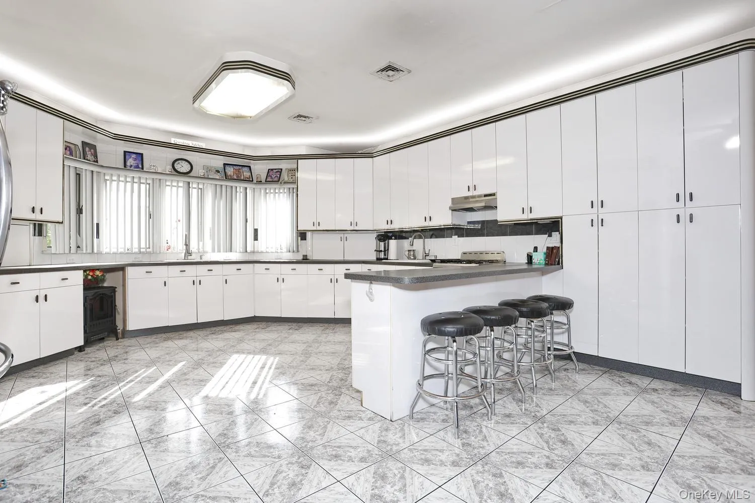 Kitchen featuring an expansive layout, white cabinetry, dark countertops, an eat-at island, and tile flooring Kitchen featuring an expansive layout, white cabinetry, dark countertops, an eat-at island, and tile flooring