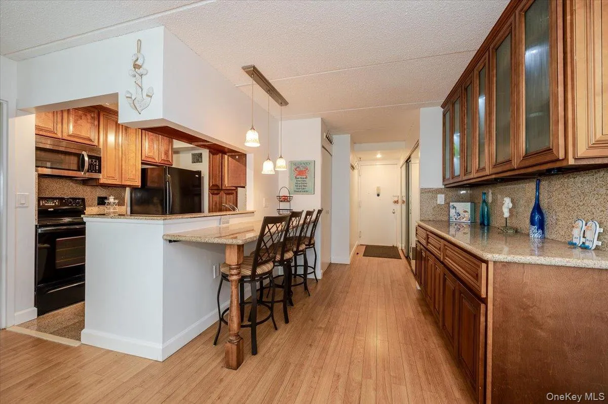 Kitchen featuring decorative backsplash, brown cabinetry, hanging light fixtures, light stone counters, and a textured ceiling Kitchen featuring decorative backsplash, brown cabinetry, hanging light fixtures, light stone counters, and a textured ceiling