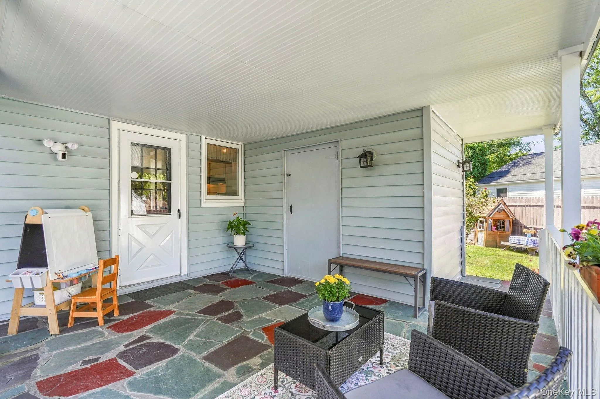 Covered patio featuring a multi-color flagstone surface, beadboard ceiling, and light-colored siding Covered patio featuring a multi-color flagstone surface, beadboard ceiling, and light-colored siding