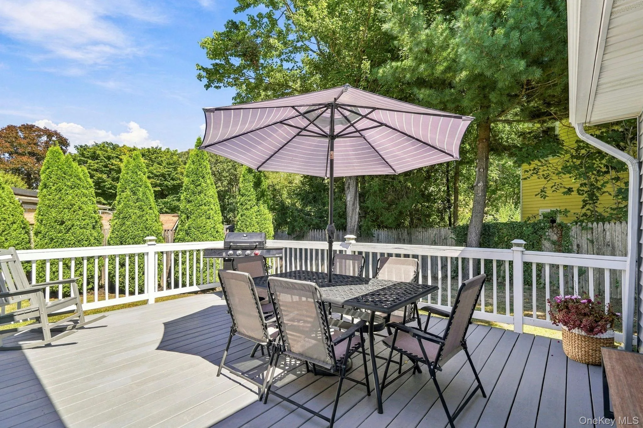 Expansive outdoor deck featuring a white railing, a gray composite surface, and mature perimeter landscaping Expansive outdoor deck featuring a white railing, a gray composite surface, and mature perimeter landscaping
