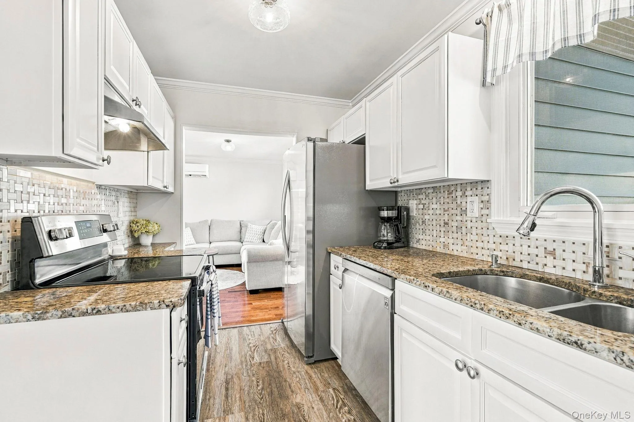 Kitchen featuring white cabinetry, stainless steel appliances, dual basin sink, wood-finish flooring, and a tiled backsplash Kitchen featuring white cabinetry, stainless steel appliances, dual basin sink, wood-finish flooring, and a tiled backsplash