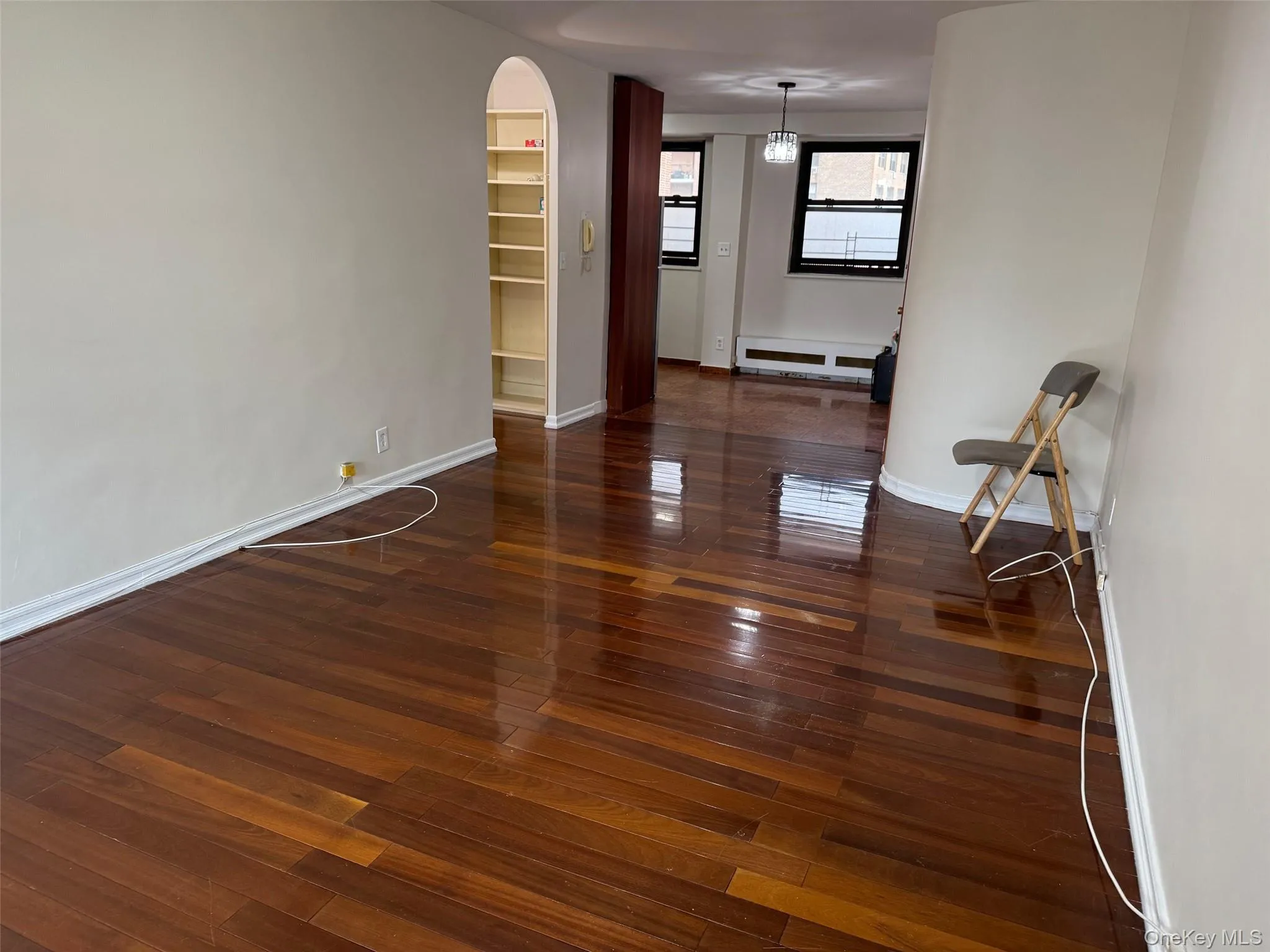 Empty room with dark wood-style floors, arched walkways, and baseboard heating Empty room with dark wood-style floors, arched walkways, and baseboard heating