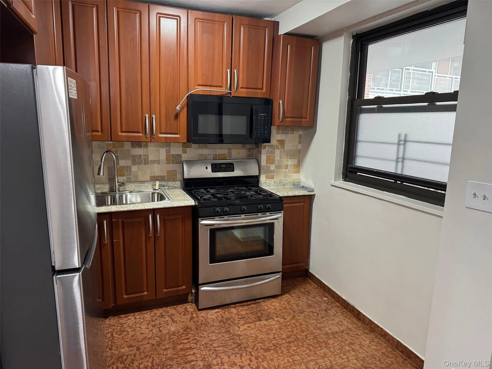 Kitchen featuring decorative backsplash, stainless steel appliances, light stone counters, and brown cabinetry Kitchen featuring decorative backsplash, stainless steel appliances, light stone counters, and brown cabinetry
