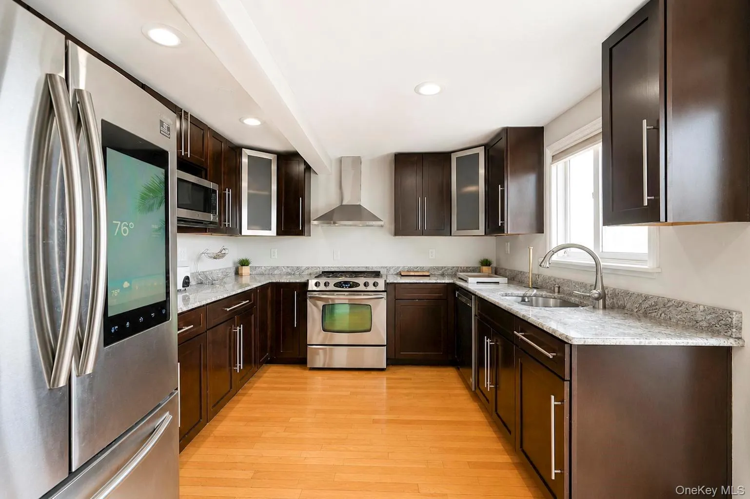U-shaped kitchen featuring dark wood cabinetry, light-toned countertops, stainless steel appliances, and wood-finish flooring U-shaped kitchen featuring dark wood cabinetry, light-toned countertops, stainless steel appliances, and wood-finish flooring