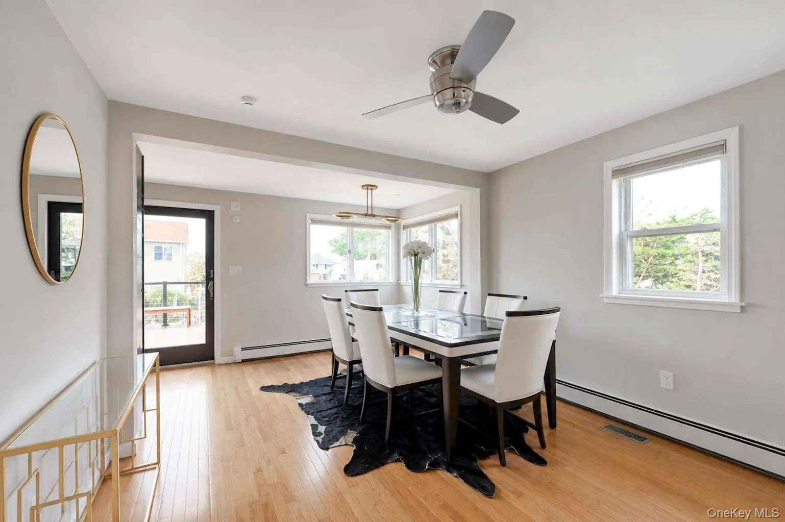 Hardwood flooring, light gray wall tones, ceiling fan, multiple windows with white trim, and a glass-paneled exterior door Hardwood flooring, light gray wall tones, ceiling fan, multiple windows with white trim, and a glass-paneled exterior door