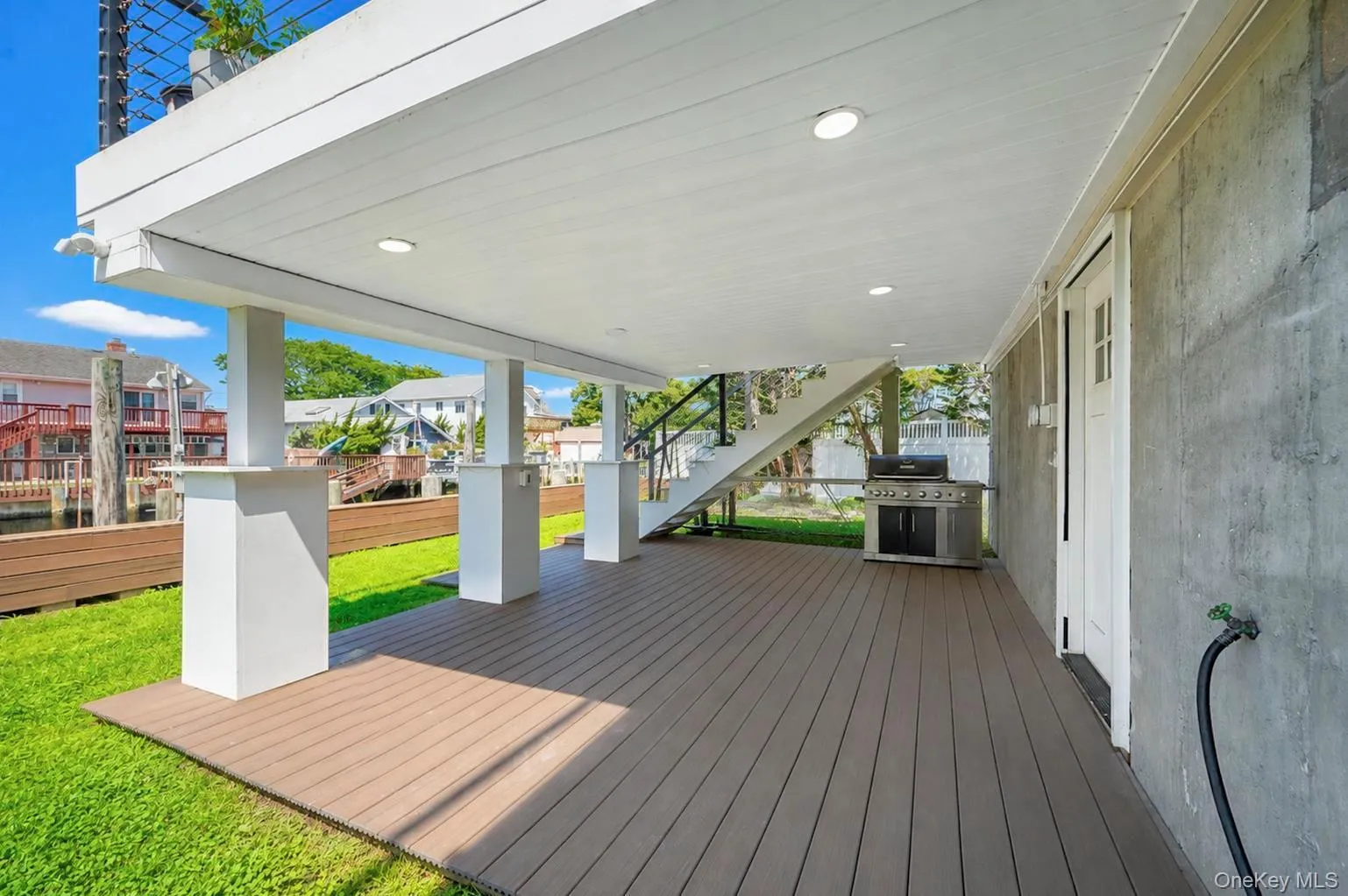 Covered outdoor deck with recessed lighting, composite decking, white support columns, and a built-in outdoor grill Covered outdoor deck with recessed lighting, composite decking, white support columns, and a built-in outdoor grill