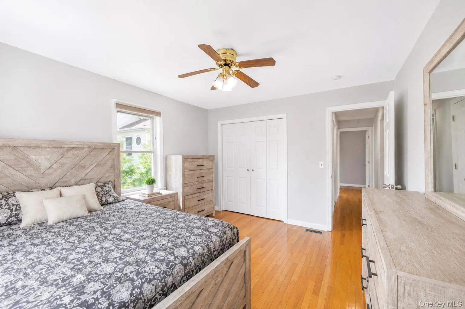 Hardwood flooring, wood-finish ceiling fan, window with exterior view, dual bi-fold closet doors, and light gray wall paint Hardwood flooring, wood-finish ceiling fan, window with exterior view, dual bi-fold closet doors, and light gray wall paint