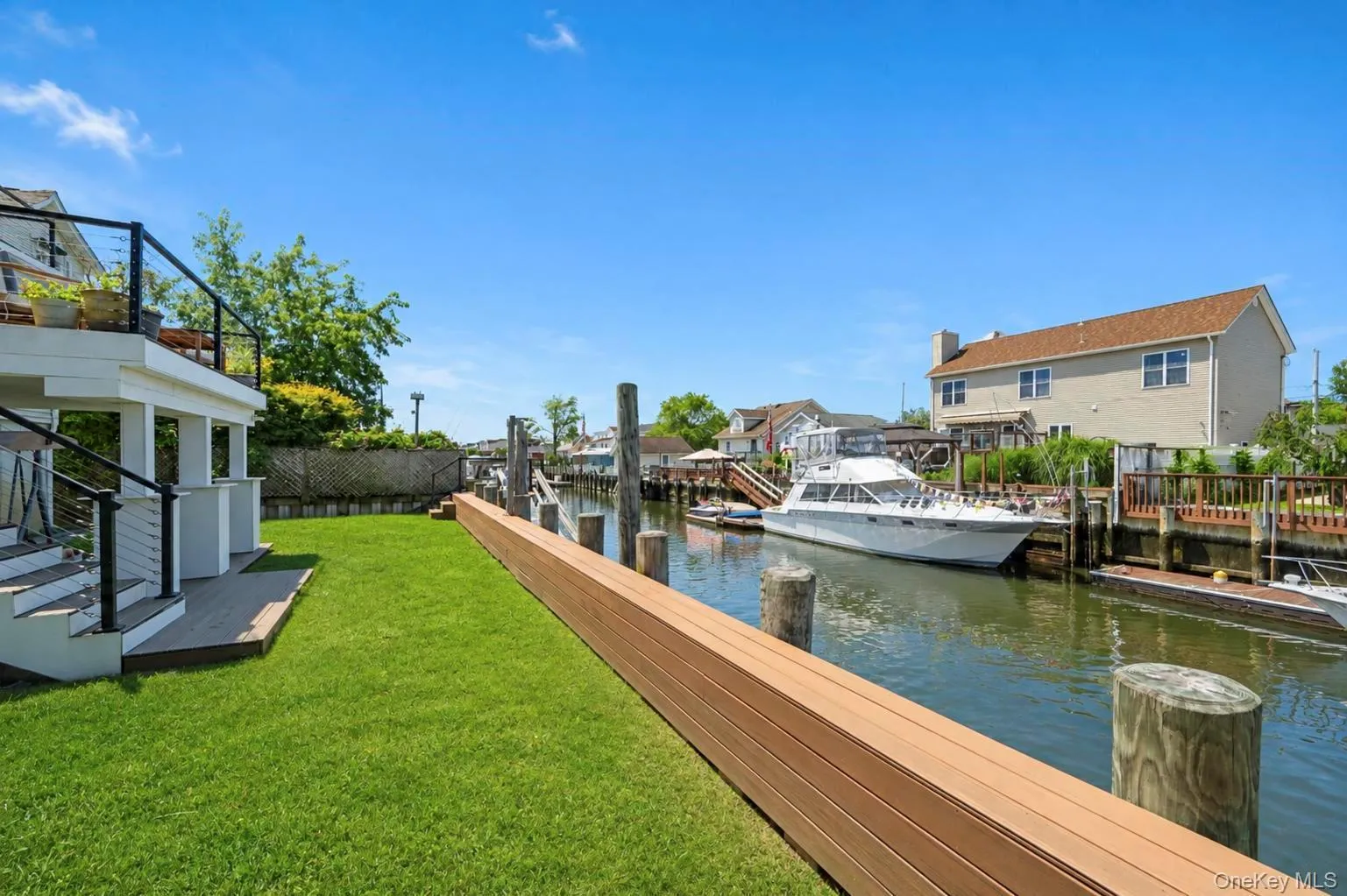 Waterfront property featuring a private boat dock, green lawn, exterior deck with railing, and adjacent waterway Waterfront property featuring a private boat dock, green lawn, exterior deck with railing, and adjacent waterway