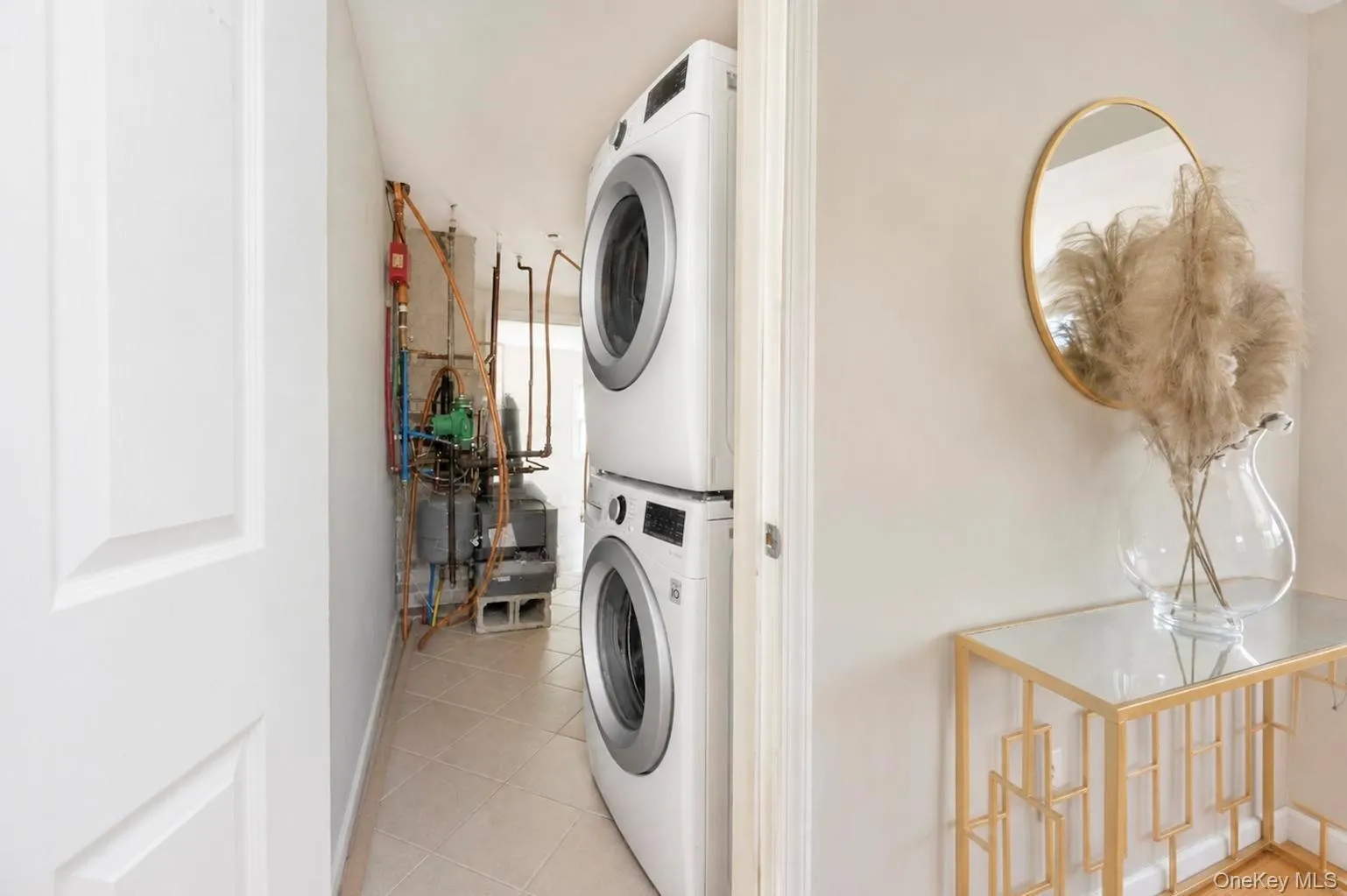 Compact laundry area featuring a stacked washer and dryer, tile flooring, and visible utility systems Compact laundry area featuring a stacked washer and dryer, tile flooring, and visible utility systems