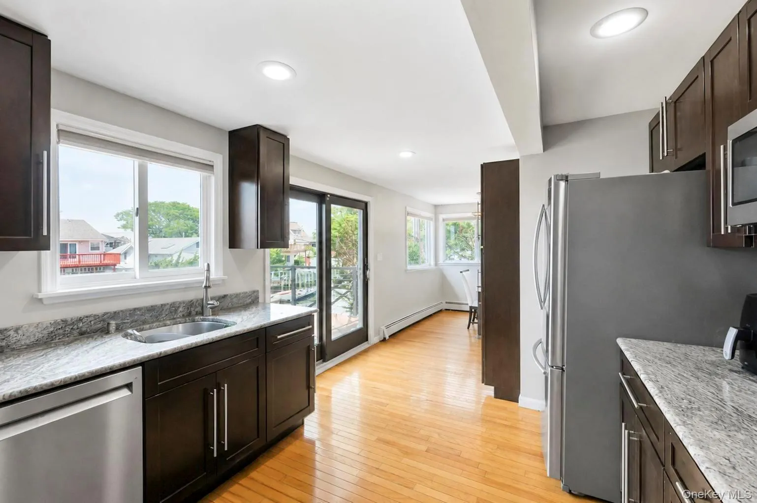 Kitchen featuring dark wood-finish cabinetry, light-toned countertops, stainless steel appliances, and a single basin sink Kitchen featuring dark wood-finish cabinetry, light-toned countertops, stainless steel appliances, and a single basin sink