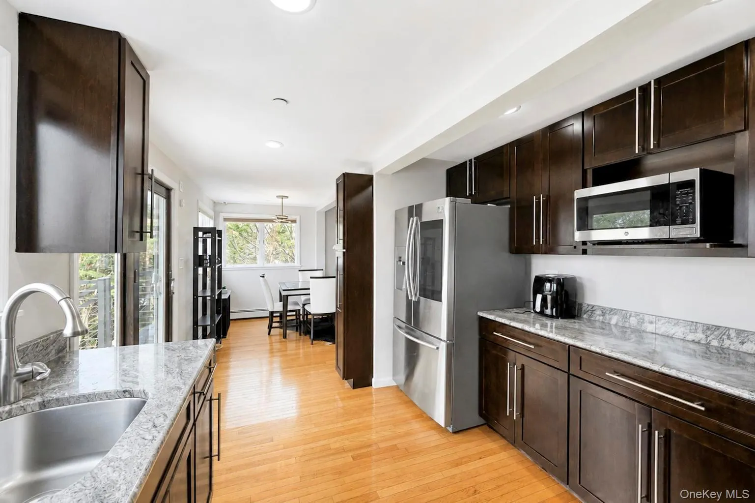 Wood-finish flooring, dark wood cabinetry, stainless steel appliances, recessed lighting, and light-toned countertops Wood-finish flooring, dark wood cabinetry, stainless steel appliances, recessed lighting, and light-toned countertops