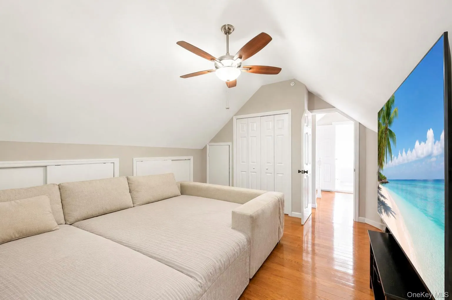 Sloped ceiling design, wood-finish flooring, ceiling fan with light, white panel closet doors, and white paneled interior doors Sloped ceiling design, wood-finish flooring, ceiling fan with light, white panel closet doors, and white paneled interior doors