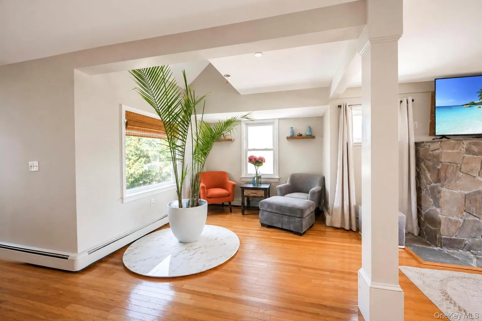 Hardwood flooring, natural light through windows with woven wood blinds, recessed lighting, and a stone-clad fireplace Hardwood flooring, natural light through windows with woven wood blinds, recessed lighting, and a stone-clad fireplace