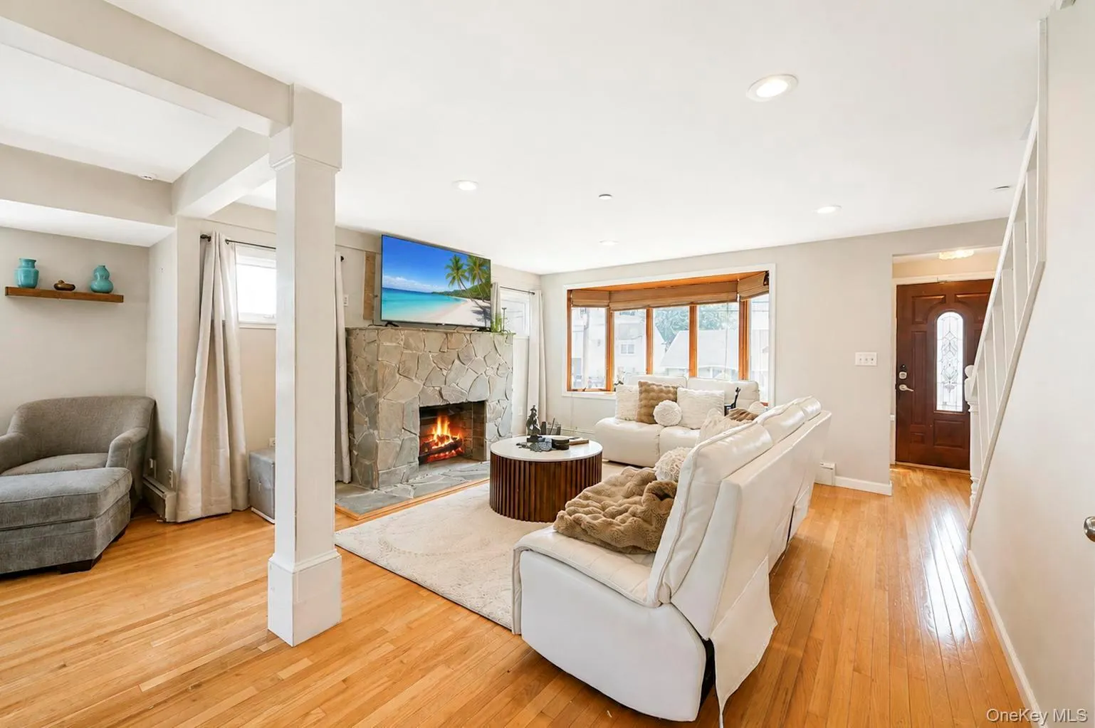 Hardwood flooring throughout, stone-clad fireplace, bay window, recessed lighting, and a paneled entry door with decorative glass Hardwood flooring throughout, stone-clad fireplace, bay window, recessed lighting, and a paneled entry door with decorative glass