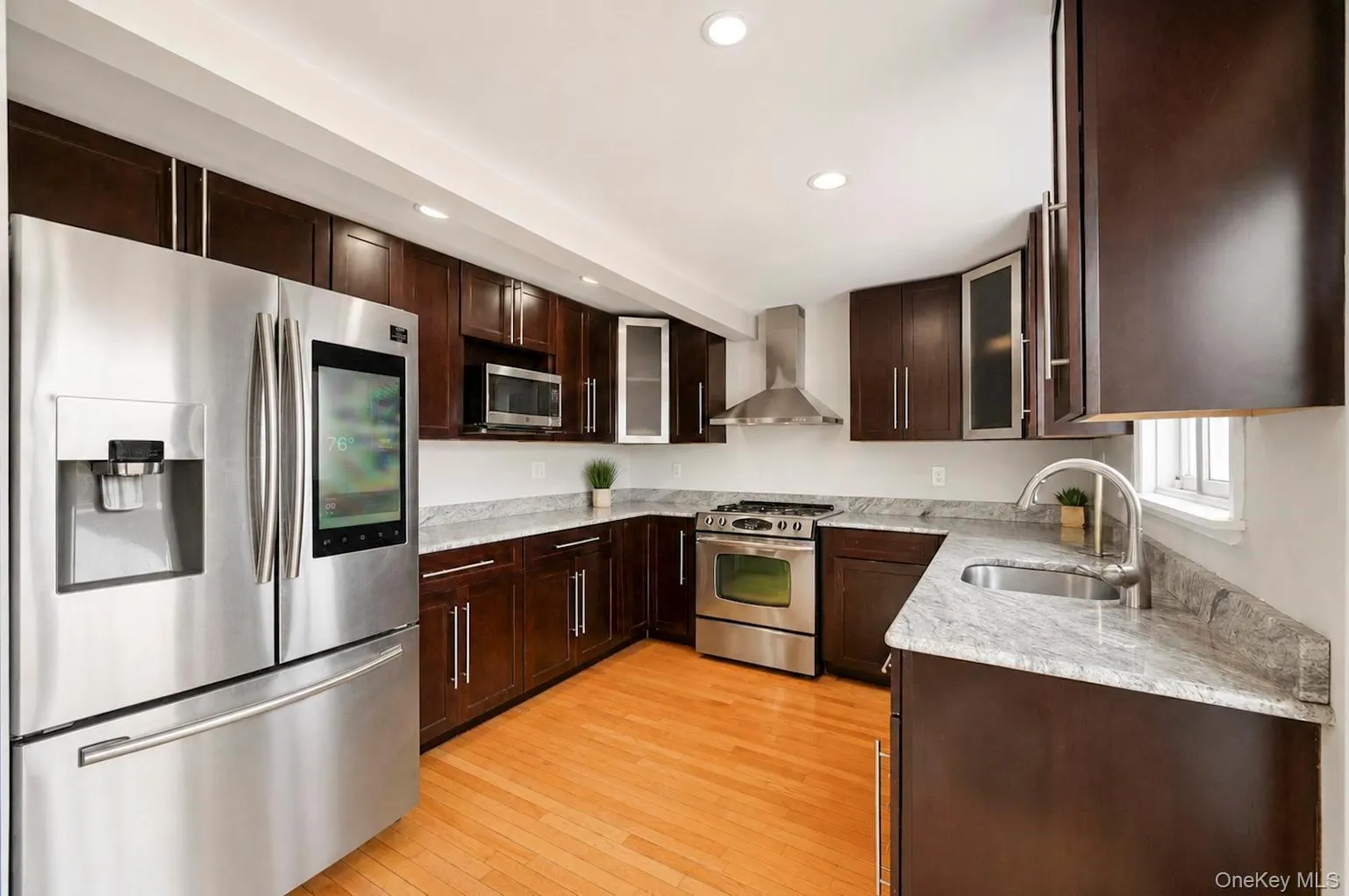 Kitchen featuring wood-finish flooring, dark wood cabinetry, stainless steel appliances, and light-toned countertops Kitchen featuring wood-finish flooring, dark wood cabinetry, stainless steel appliances, and light-toned countertops